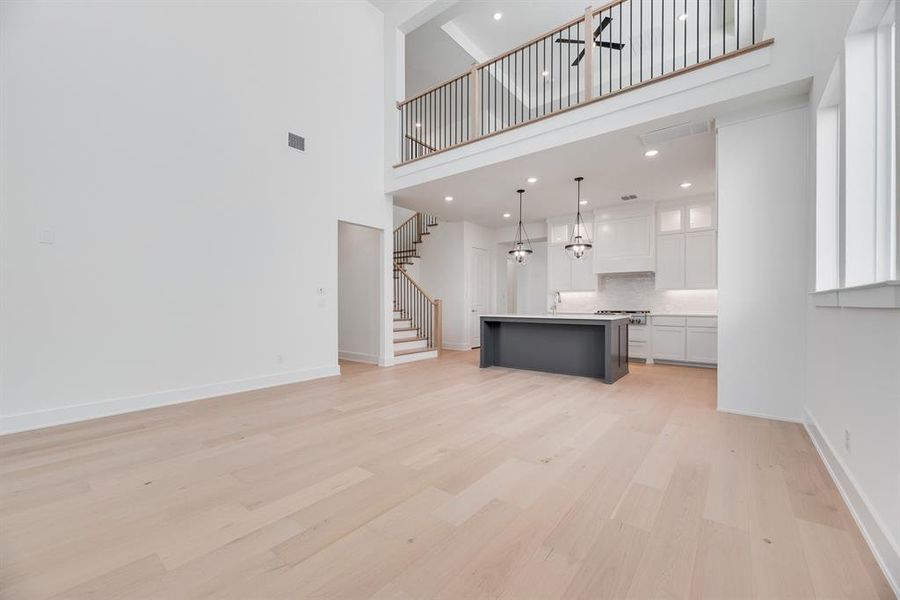 Unfurnished living room with light wood-style floors, a high ceiling, stairway, and recessed lighting