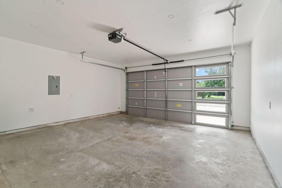 A clean, spacious 8-foot-ceiling garage featuring a contemporary overhead garage door with glass panels that allow natural light to flow in. Ideal for parking, storage, or even a home workshop.