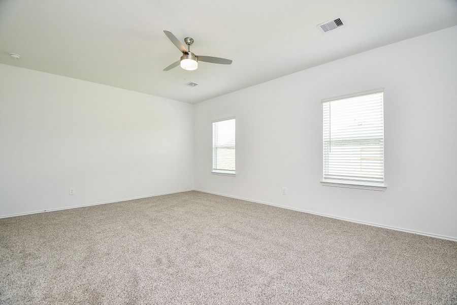 This spacious bedroom features neutral carpeting, two large windows with blinds for natural light, and a modern ceiling fan, creating a comfortable and inviting atmosphere.