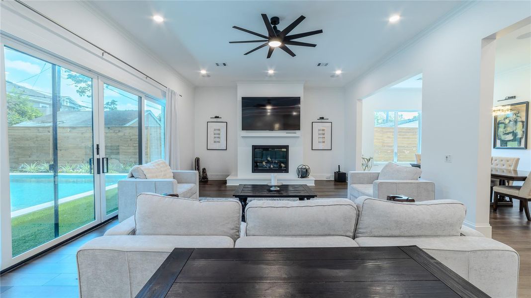 This spacious living room features contemporary furnishings, a cozy fireplace, and a mounted TV. Large sliding glass doors open to a backyard with a pool, providing abundant natural light and a seamless indoor-outdoor flow.