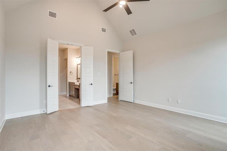 Unfurnished bedroom featuring light wood-type flooring, connected bathroom, ceiling fan, and high vaulted ceiling