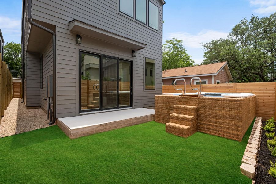 A private backyard oasis features a hot tub, artificial turf, and a sleek modern exterior with sliding glass doors.