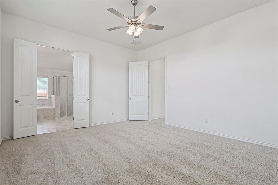 Unfurnished bedroom with connected bathroom, light carpet, and ceiling fan