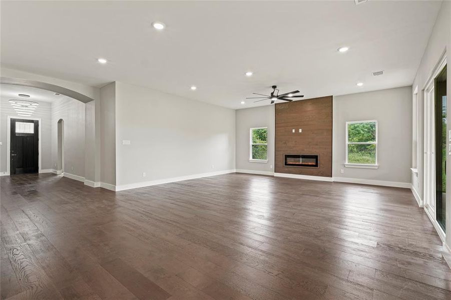 Living room featuring ceiling fan, arched walkways, recessed lighting, a large fireplace, and dark wood-style floors