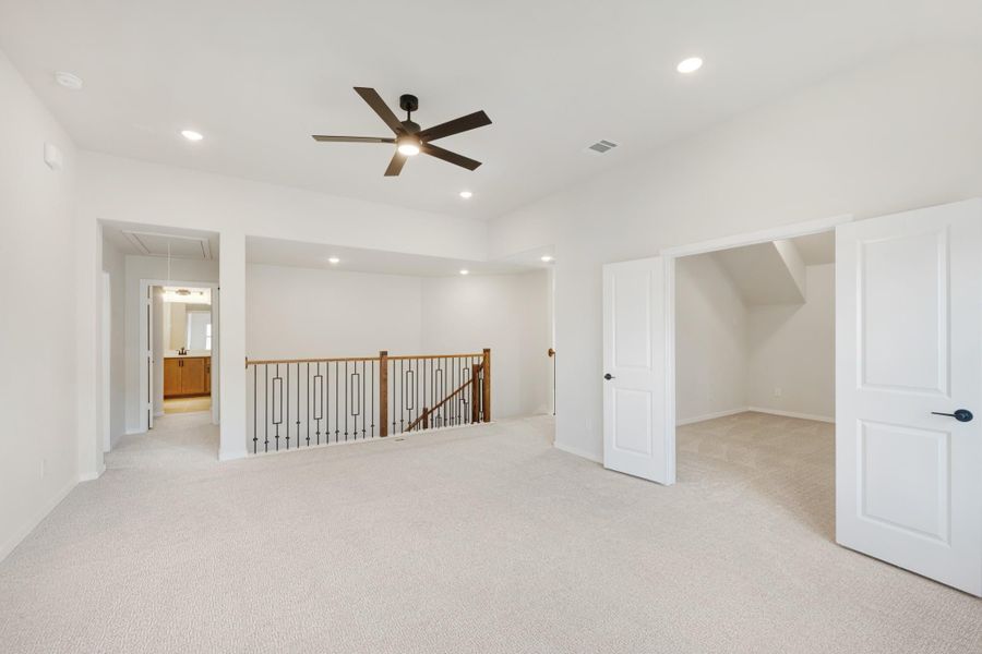 Spacious upstairs loft with carpet, ceiling fan, iron stair railing, and open doorways to bathroom and closet.