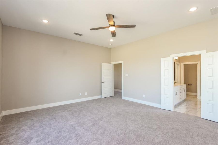 Unfurnished bedroom featuring ceiling fan, ensuite bathroom, and light carpet