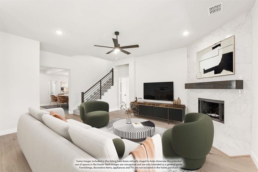 Living room with marble fireplace, ceiling fan, white sofa, and green accent chairs near open staircase