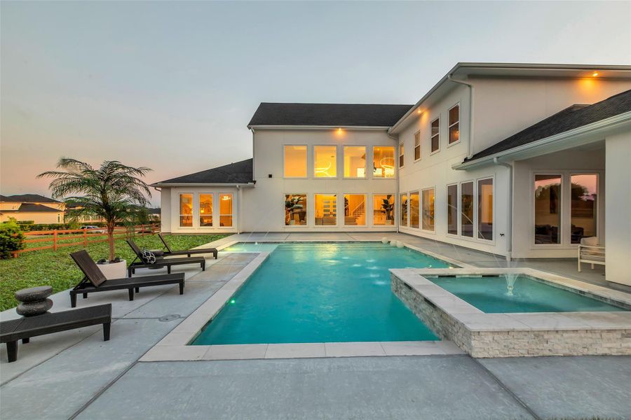 Resort-Style Escape: The backyard transforms into a private oasis with a glowing pool and elevated spa accented by illuminated fountains. Surrounded by multiple walls of glass, the interior seamlessly connects to the outdoors, creating an ideal setting for both tranquil evenings and sophisticated entertaining under the stars.