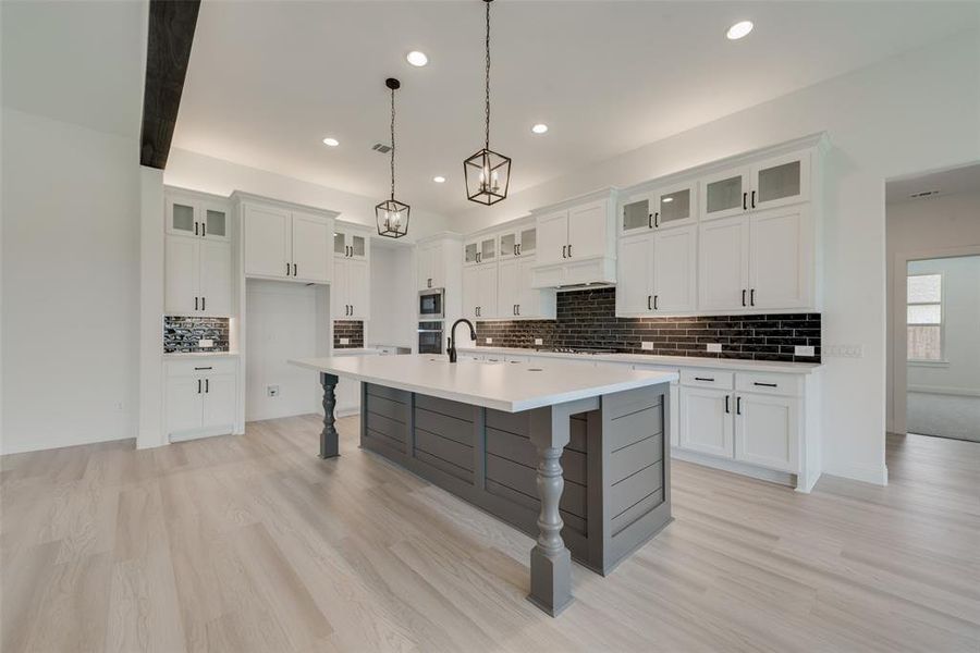 Kitchen with white cabinetry, decorative backsplash, and a kitchen island with sink