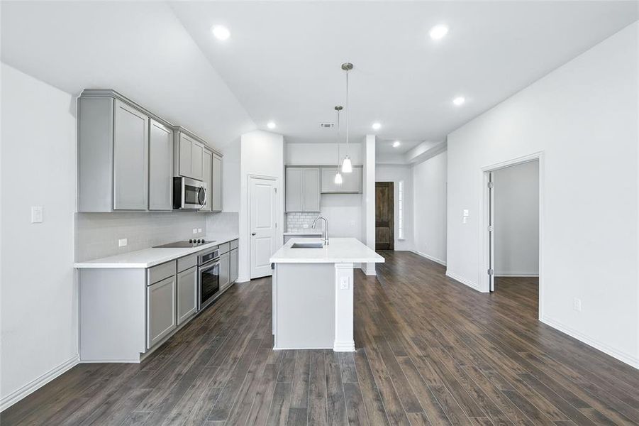 Kitchen with gray cabinetry, backsplash, an island with sink, decorative light fixtures, and dark wood-style floors Kitchen with gray cabinetry, backsplash, an island with sink, decorative light fixtures, and dark wood-style floors
