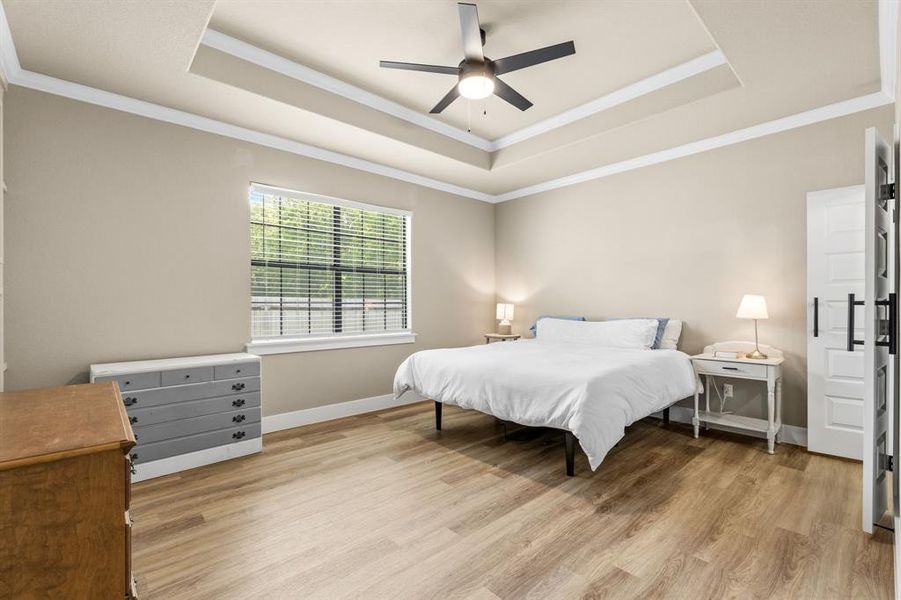 Spacious room featuring a tray ceiling with a ceiling fan, recessed window with blinds, wood-finish flooring, and crown molding