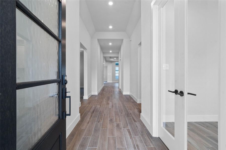 Step inside to a bright interior entryway. The space is accentuated by high ceilings and gorgeous wood-look tile flooring. The hallway extends toward large windows at the rear, flooding the area with natural light.