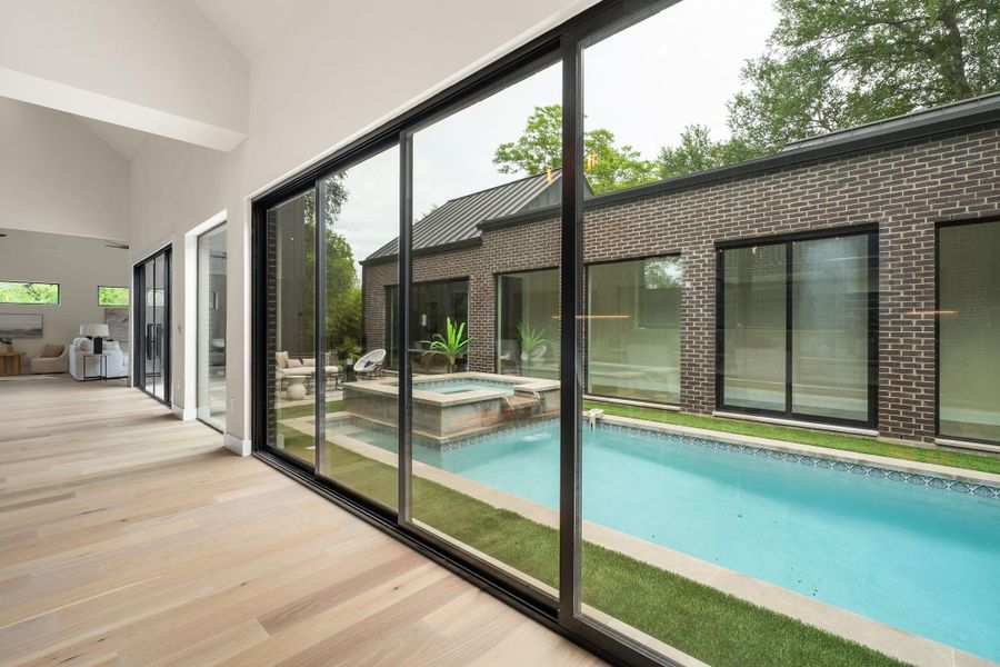 Expansive sliding glass doors overlook a rectangular swimming pool with integrated spa