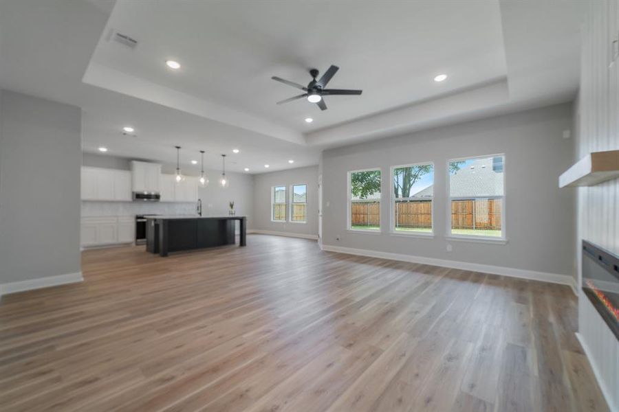 Unfurnished living room featuring light hardwood / wood-style floors, ceiling fan, and a tray ceiling