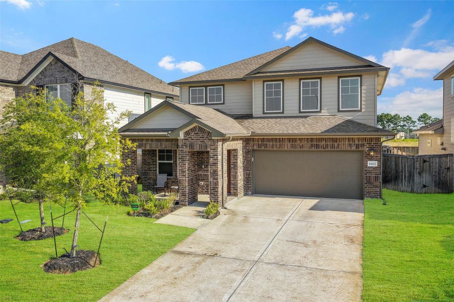 Charming two-story home with a brick facade, spacious two-car garage, and inviting front porch, set on a well-maintained lawn in a desirable neighborhood.