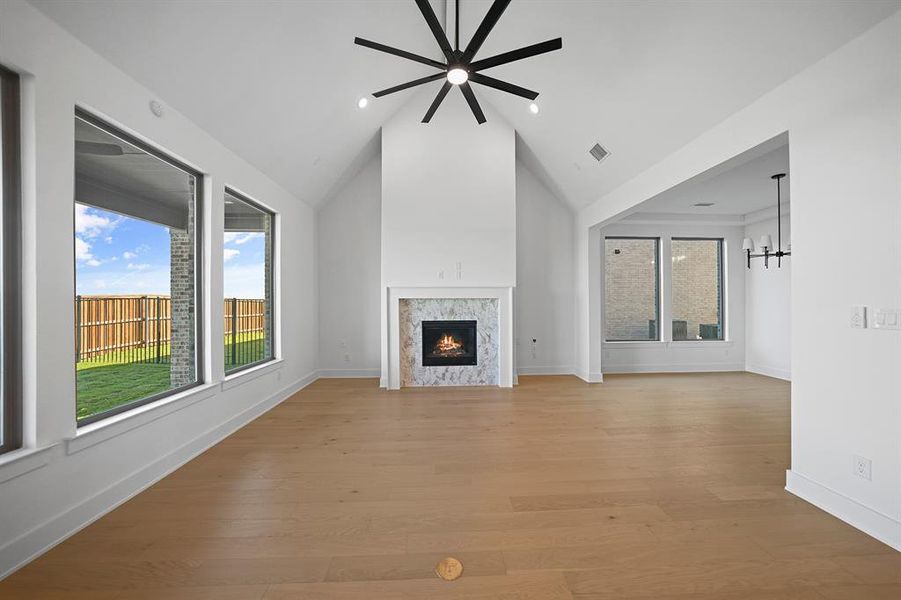 Unfurnished living room with light wood finished floors, a premium fireplace, high vaulted ceiling, a chandelier, and recessed lighting