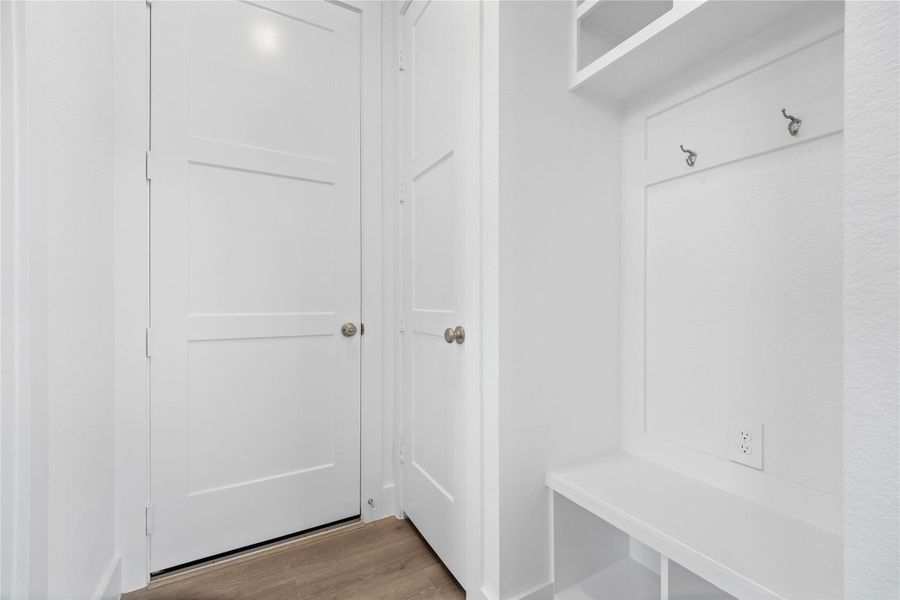 Step into this highly functional and stylish mudroom drop zone, an essential feature for a busy household. The space boasts custom-built white cabinetry and shelving, providing generous storage for coats, bags, and shoes. A comfortable built-in bench offers a convenient spot to sit, while three sleek hooks keep outerwear tidy and accessible.