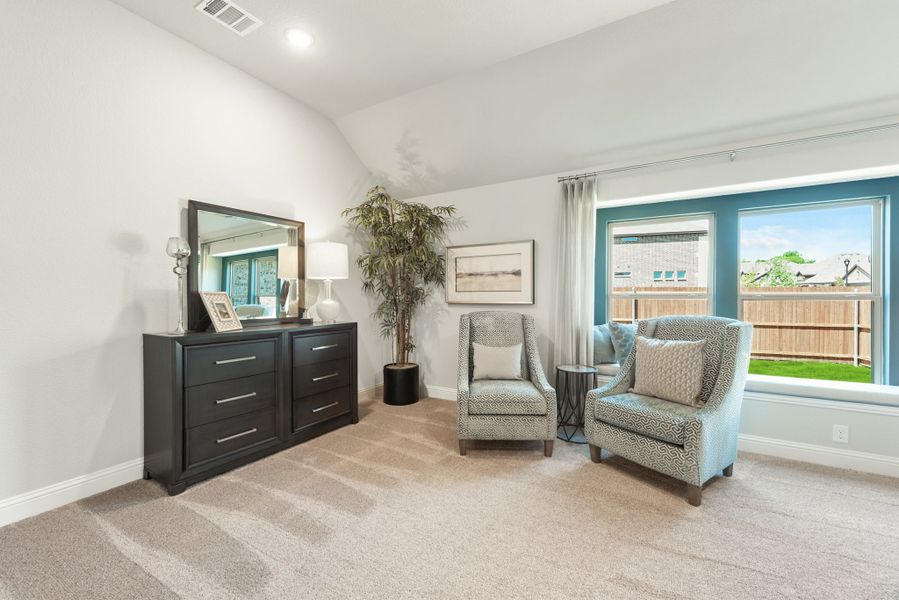 Bedroom sitting area with two accent chairs, dark dresser with mirror, and large window with backyard view