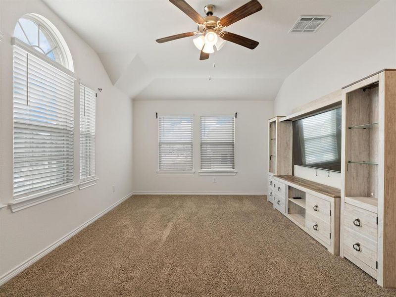 Unfurnished living room with ceiling fan, vaulted ceiling, and carpet