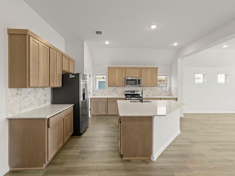 Kitchen featuring a central island, light wood-finish cabinetry, light countertops, integrated stainless steel appliances, and wood-finish flooring
