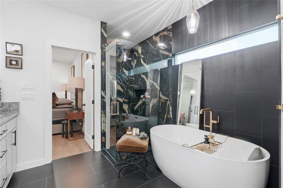 Contemporary bathroom featuring a freestanding soaking tub, a glass-enclosed shower with black marble-effect wall tiling, dark large format floor tiles, and a transom window