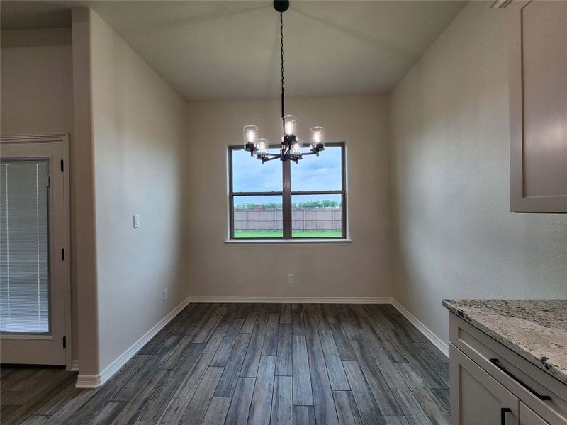 Dining area featuring wood-finish flooring, a contemporary chandelier, and a window overlooking a fenced yard