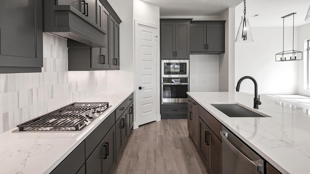 Kitchen with stainless steel appliances, tasteful backsplash, light stone countertops, light wood finished floors, and pendant lighting Kitchen with stainless steel appliances, tasteful backsplash, light stone countertops, light wood finished floors, and pendant lighting