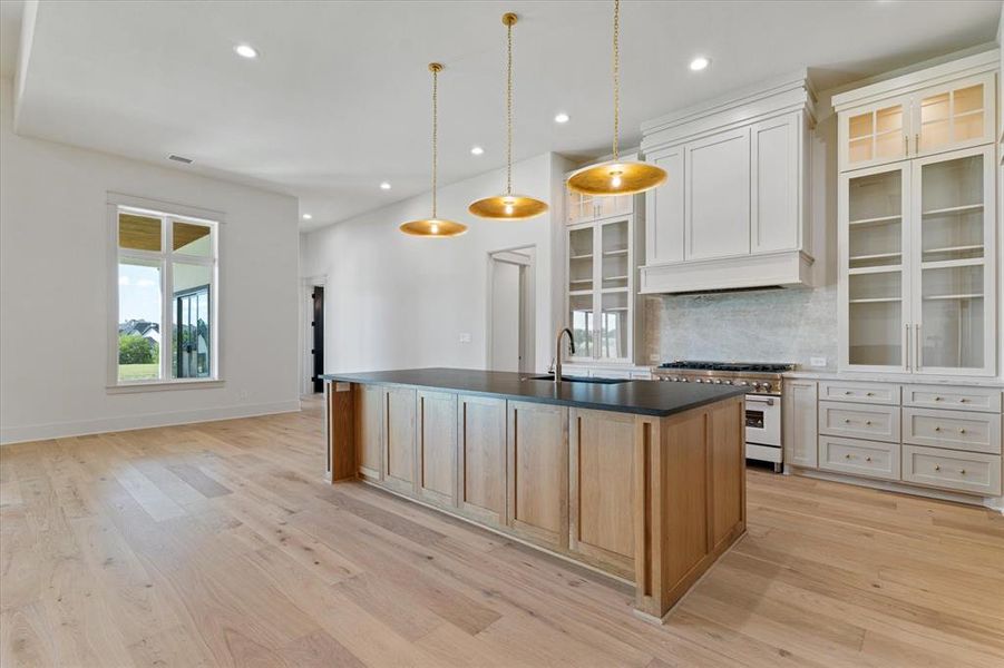 Kitchen with double oven range, a center island with sink, recessed lighting, tasteful backsplash, and dark countertops