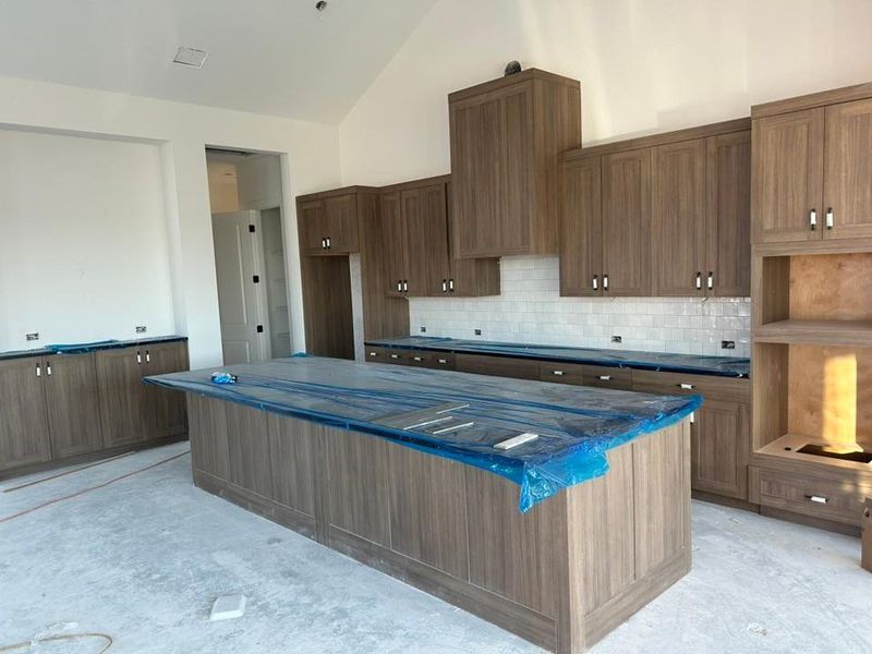 Kitchen featuring brown cabinetry, decorative backsplash, a large island, a breakfast bar area, and high vaulted ceiling Kitchen featuring brown cabinetry, decorative backsplash, a large island, a breakfast bar area, and high vaulted ceiling