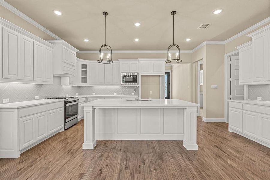 Kitchen with stainless steel gas stove, decorative backsplash, black microwave, light wood-type flooring, and white cabinets