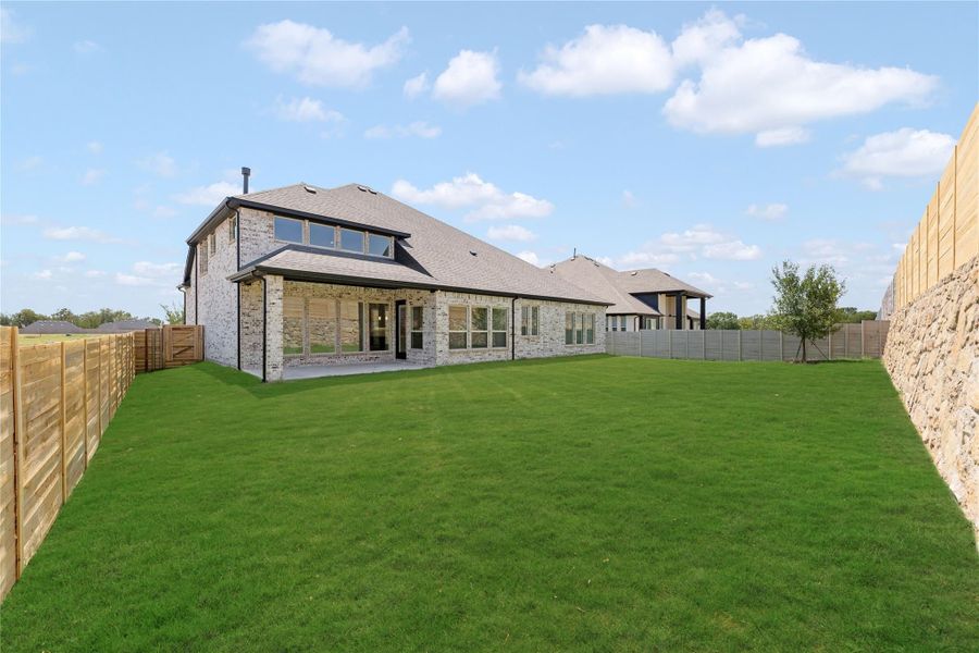 Rear view of brick home with large fenced backyard, covered patio, and tall windows