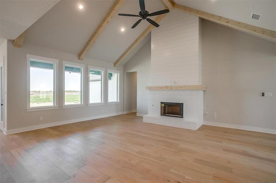 Unfurnished living room featuring visible vents, a brick fireplace, beamed ceiling, light wood finished floors, and high vaulted ceiling Unfurnished living room featuring visible vents, a brick fireplace, beamed ceiling, light wood finished floors, and high vaulted ceiling