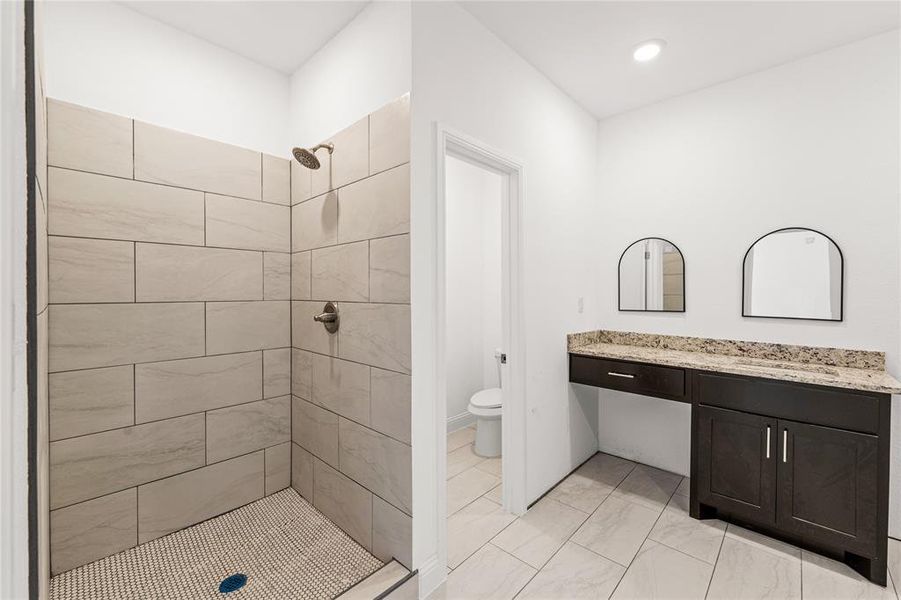 Bathroom featuring tiled shower, vanity, and toilet