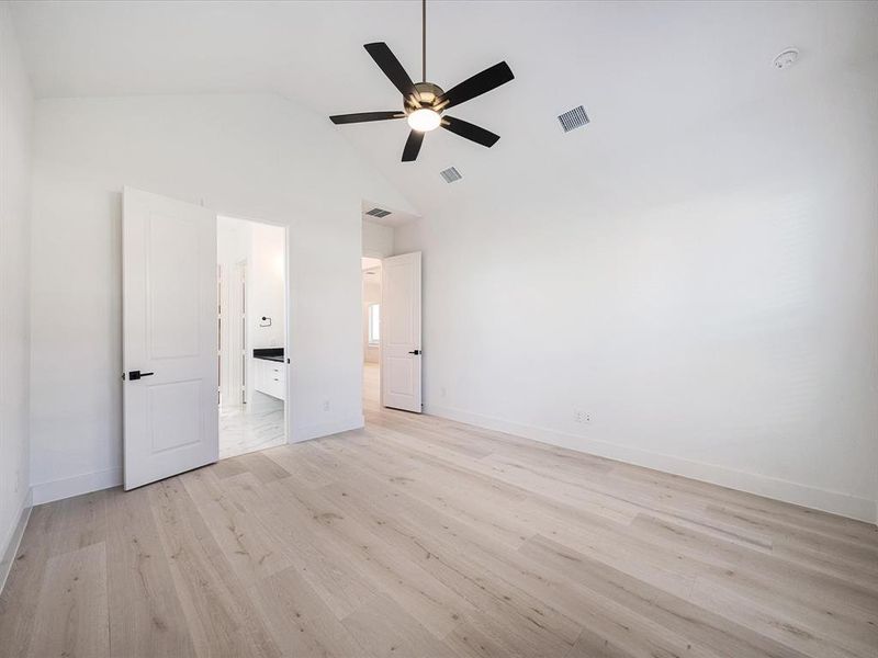 Unfurnished bedroom featuring light wood-style flooring, ensuite bath, ceiling fan, and high vaulted ceiling