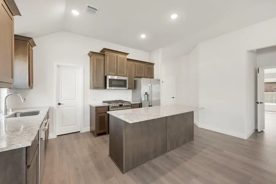 Kitchen with dark wood cabinets, granite island, stainless steel appliances, and light hardwood floors Kitchen with dark wood cabinets, granite island, stainless steel appliances, and light hardwood floors