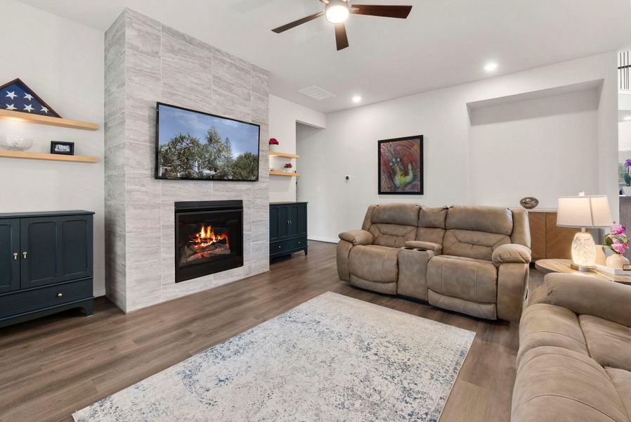 Living area featuring a floor-to-ceiling tiled fireplace, wood-finish flooring, recessed lighting, a ceiling fan, and floating wall shelves