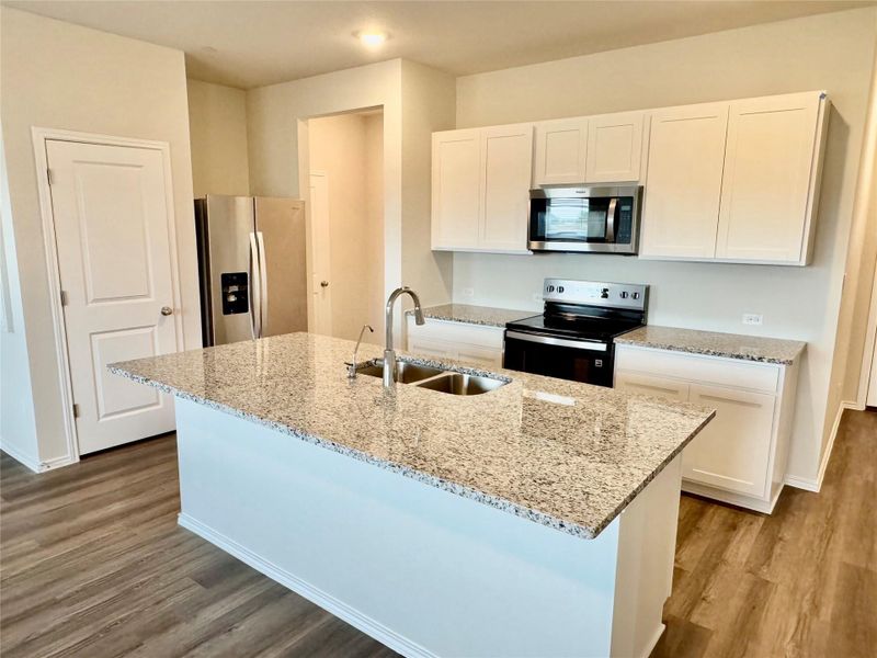 Kitchen with stainless steel appliances, white cabinetry, light stone counters, and a center island with sink