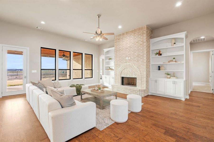 Living room with a brick fireplace, built in features, ceiling fan, and light hardwood / wood-style flooring