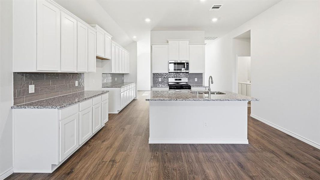 Kitchen featuring light stone counters, white cabinets, dark wood-style floors, an island with sink, and recessed lighting