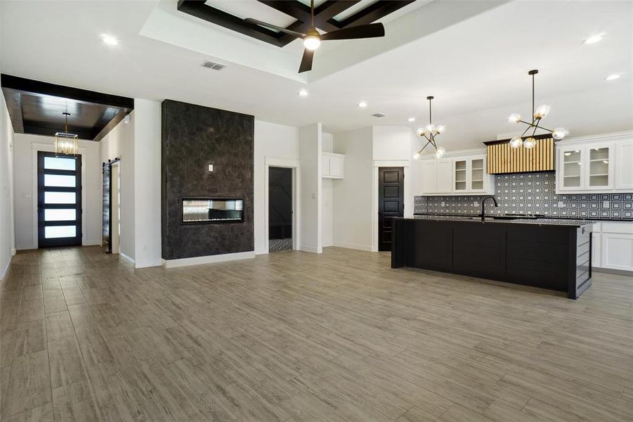 Kitchen with decorative light fixtures, a tray ceiling, ceiling fan with notable chandelier, white cabinets, and a kitchen island with sink