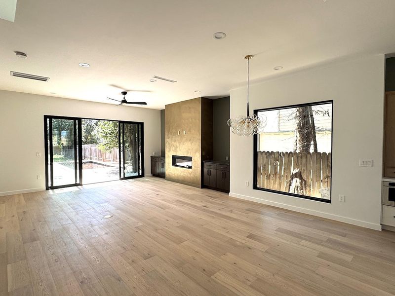 Unfurnished living room featuring visible vents, baseboards, a fireplace, light wood-style floors, and ceiling fan with notable chandelier