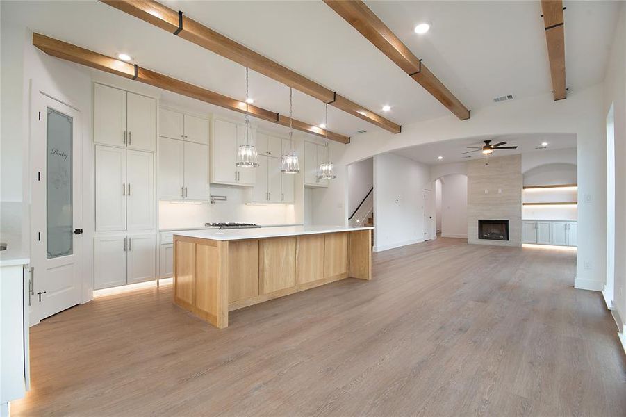 Kitchen featuring white cabinets, hanging light fixtures, a spacious island, a ceiling fan, and beam ceiling