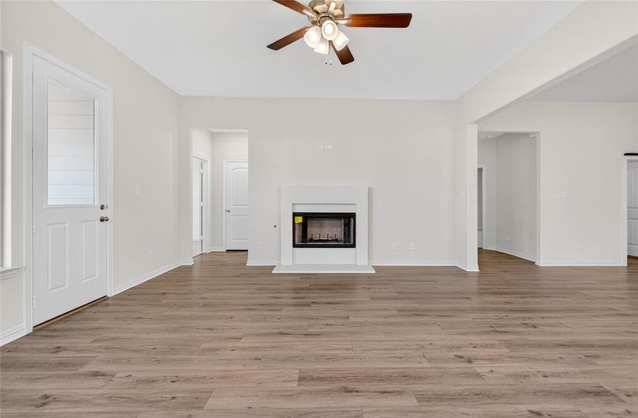 Unfurnished living room featuring a fireplace with raised hearth, ceiling fan, and light wood-style flooring