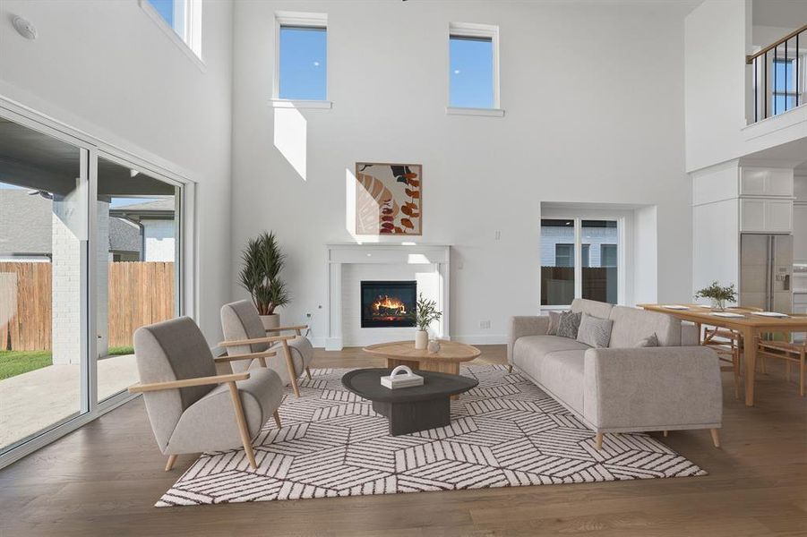 Living room with a warm lit fireplace, a towering ceiling, and wood finished floors Living room with a warm lit fireplace, a towering ceiling, and wood finished floors