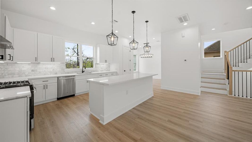 Masterfully equipped kitchen featuring a large island, beautiful tile backsplash, under cabinet lighting and outlets, granite countertops, soft close cabinets and drawers, and pot filler.