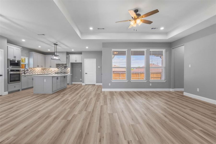 Unfurnished living room featuring a tray ceiling, a ceiling fan, visible vents, and recessed lighting
