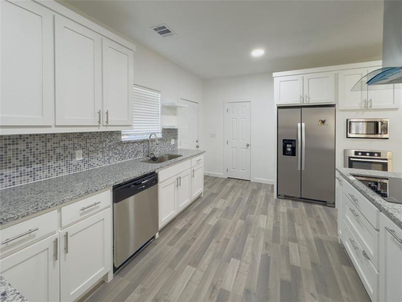 Kitchen with wall chimney exhaust hood, sink, white cabinetry, and appliances with stainless steel finishes