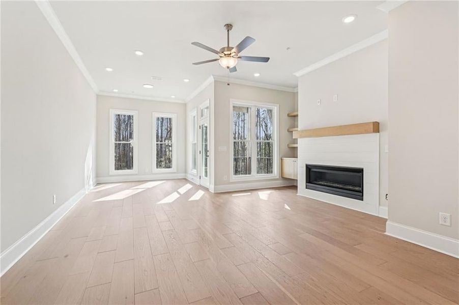 Unfurnished living room featuring ceiling fan, a glass covered fireplace, ornamental molding, recessed lighting, and light wood finished floors