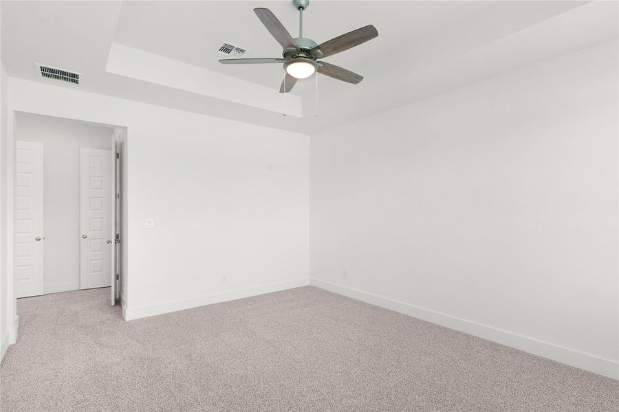 Carpeted spare room featuring a ceiling fan and a raised ceiling