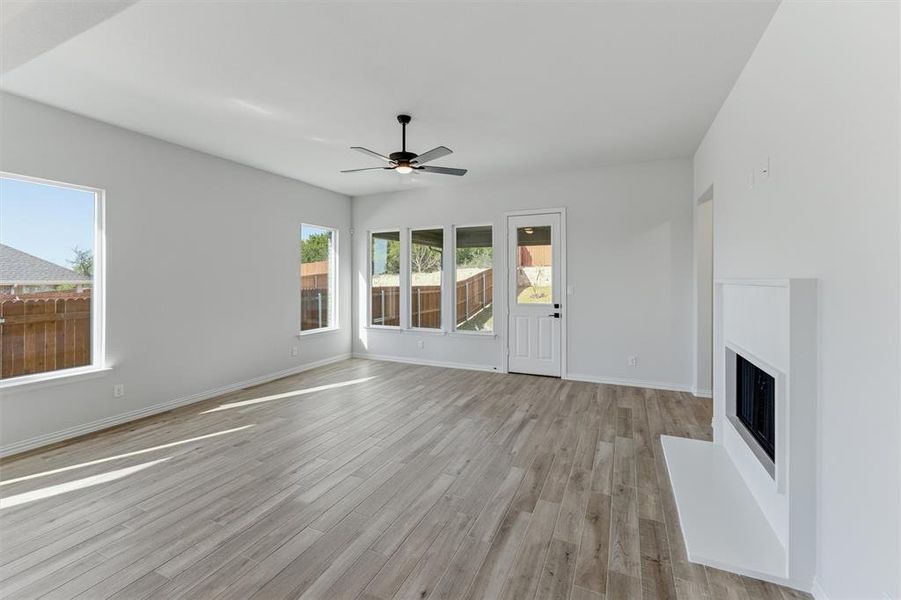 Unfurnished living room featuring ceiling fan, light wood finished floors, and a fireplace with raised hearth